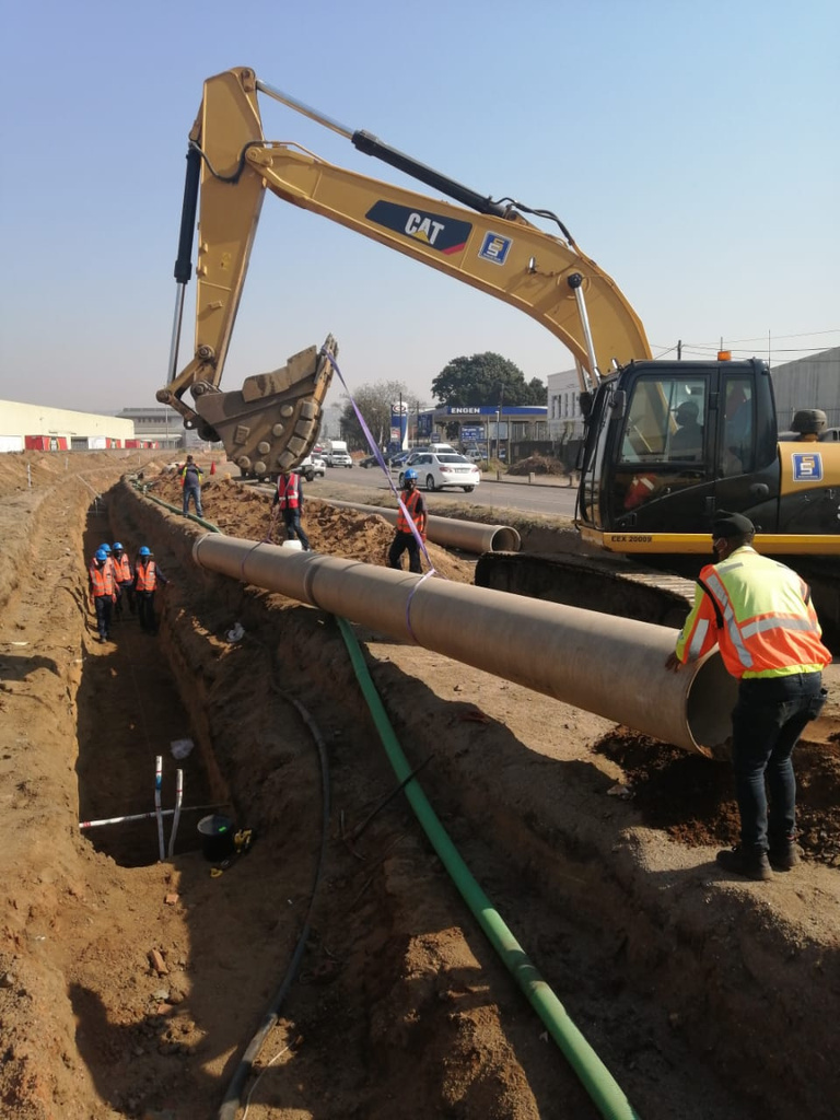 Excavator lowering a large pipe into a trench
